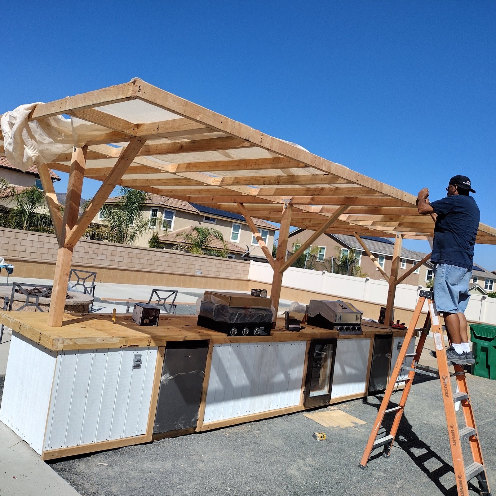 Outdoor kitchen and pergola frame going up under a blue sky